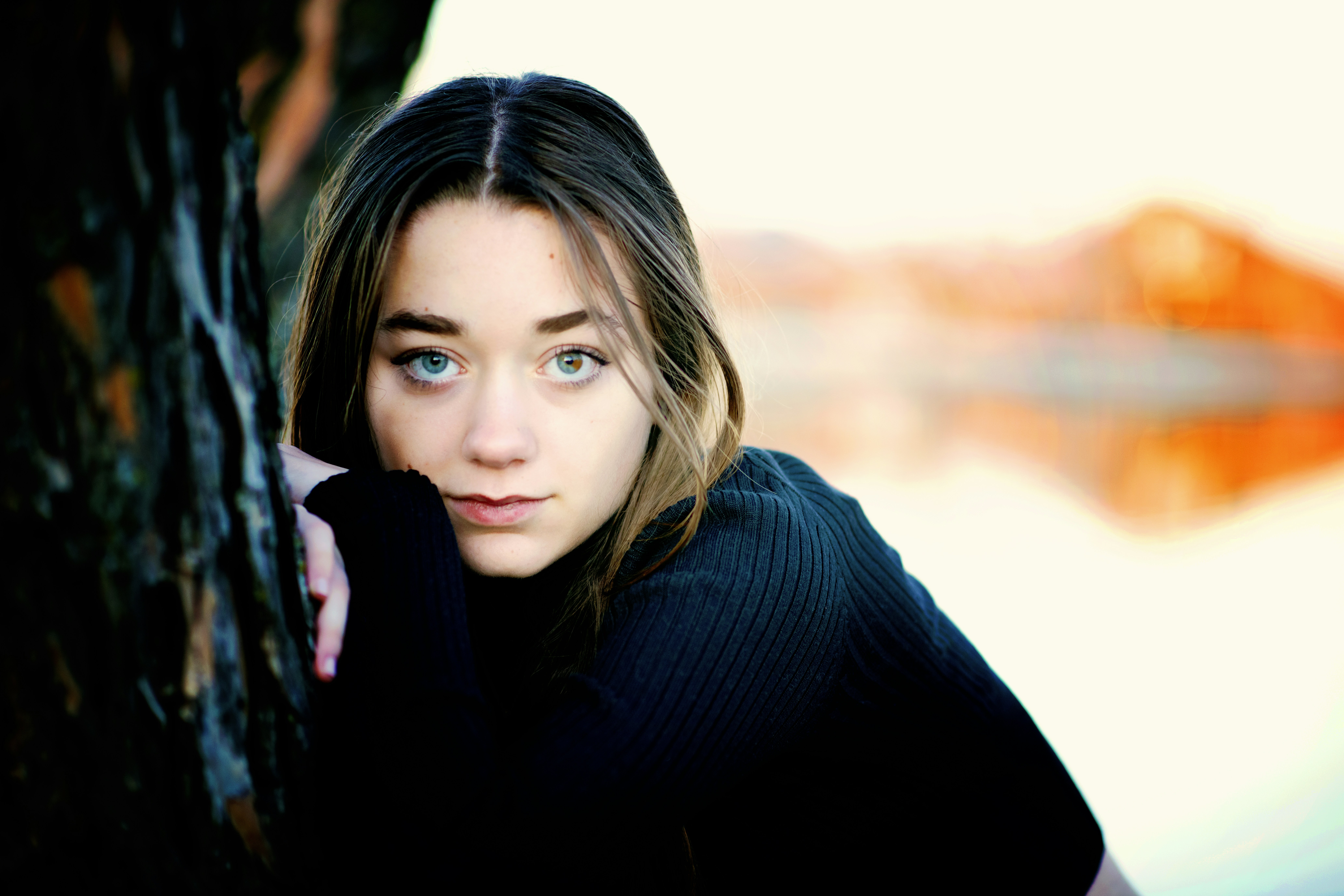 A beautiful young woman leaning against a tree