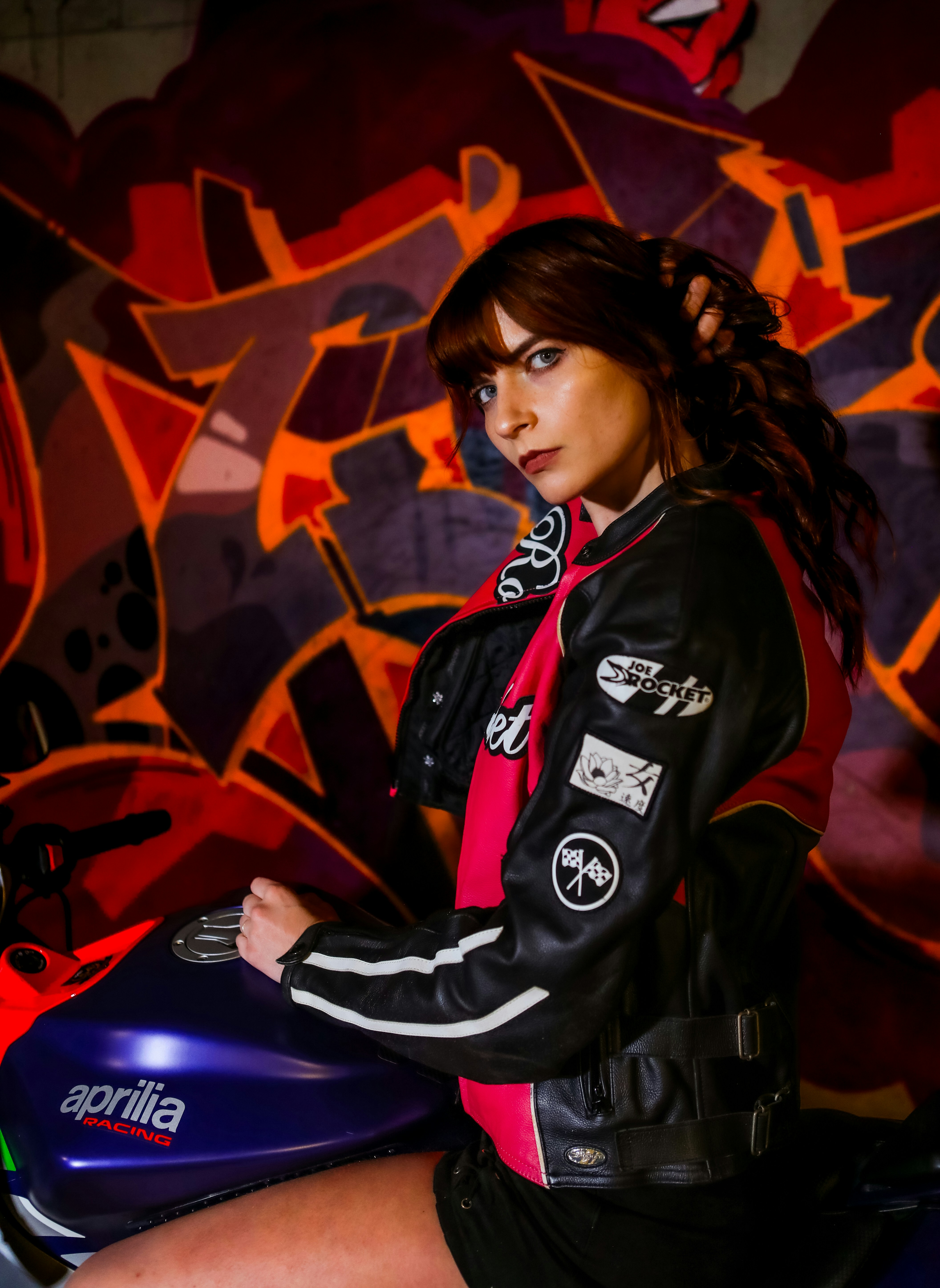 Une femme assise sur une moto devant un mur de graffitis