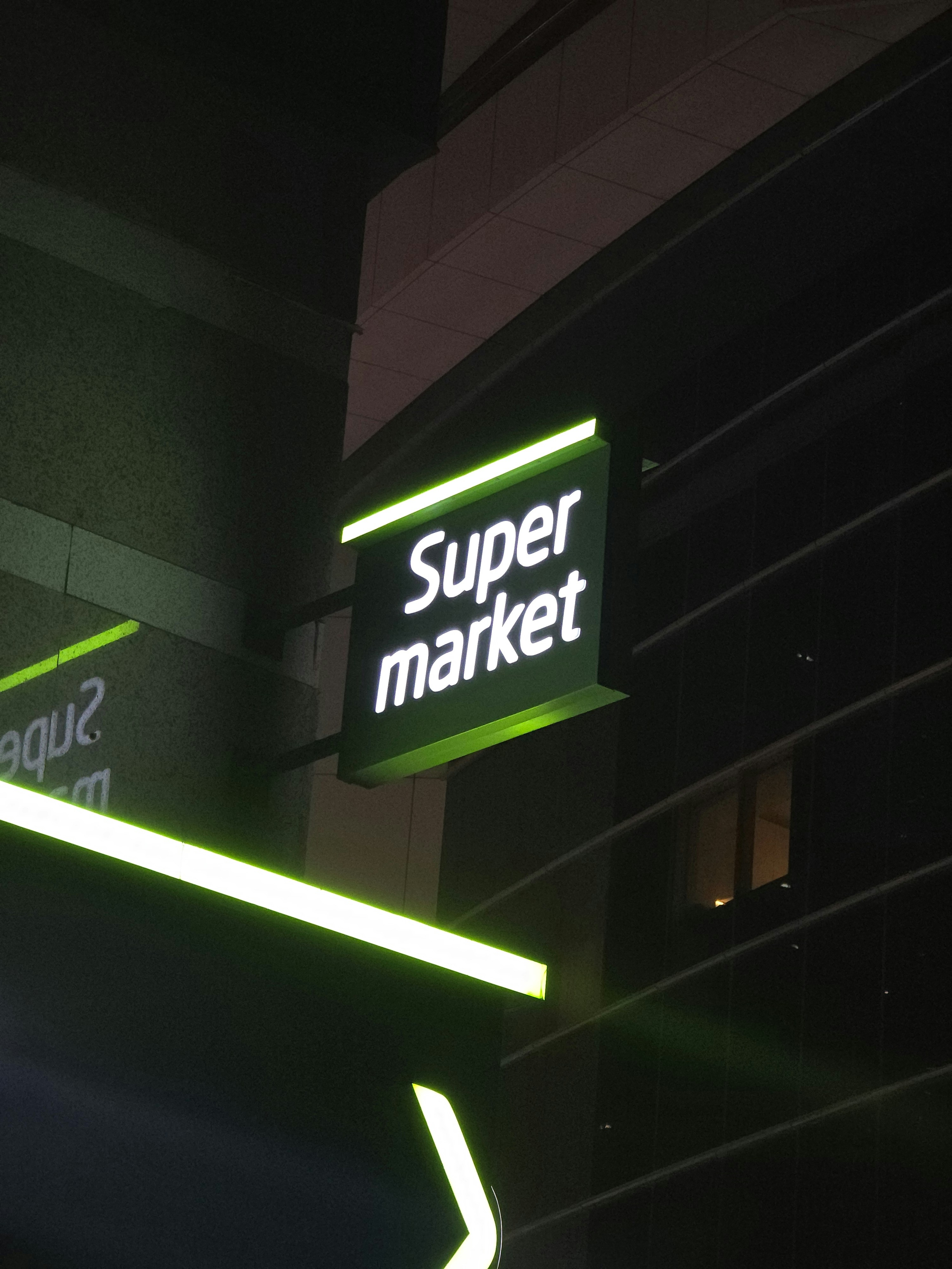 A neon sign that reads super market hanging from the side of a building