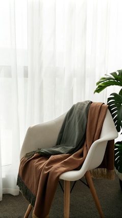 A chair with a blanket on it in front of a window