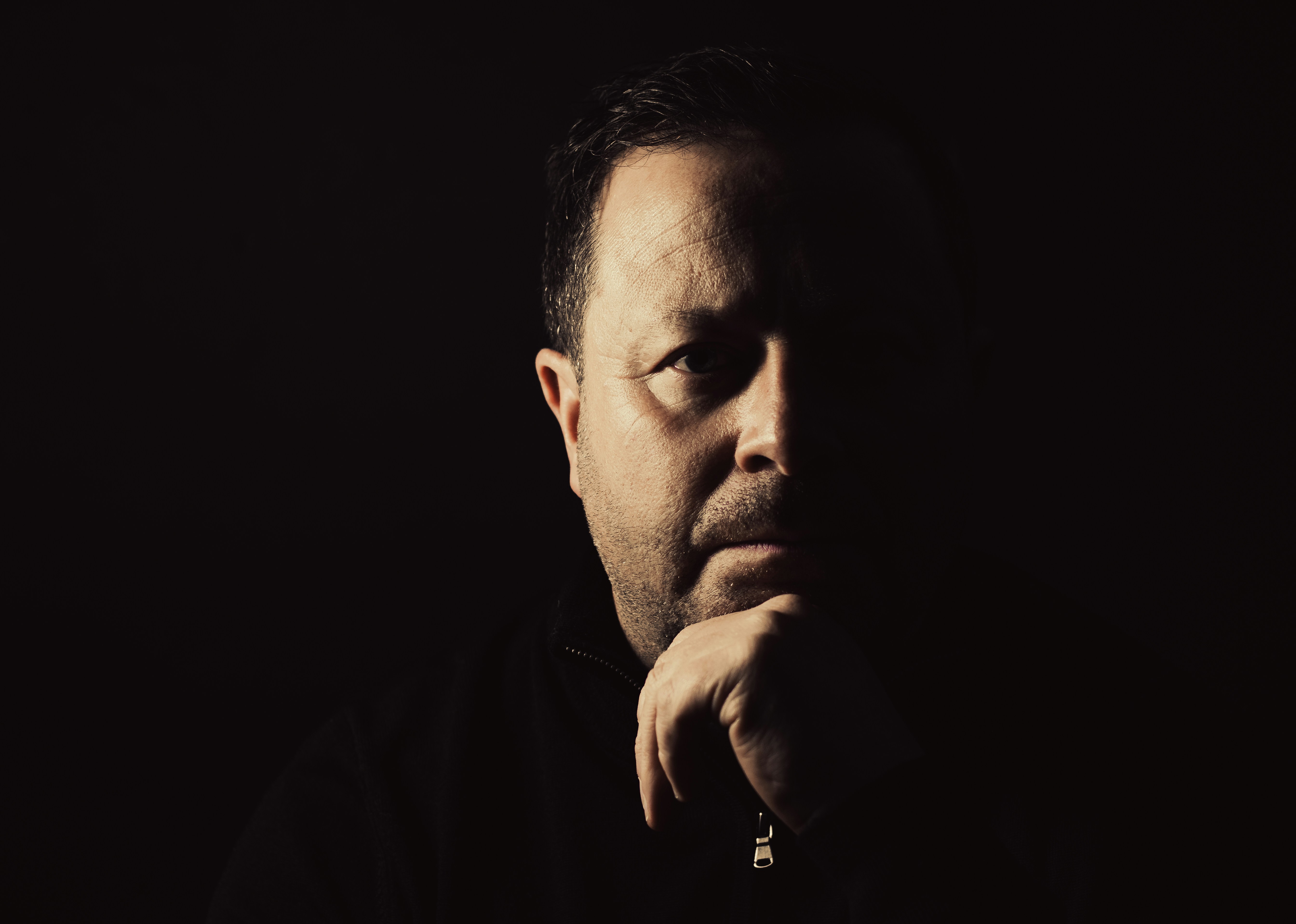 A man sitting in the dark with his hand on his chin