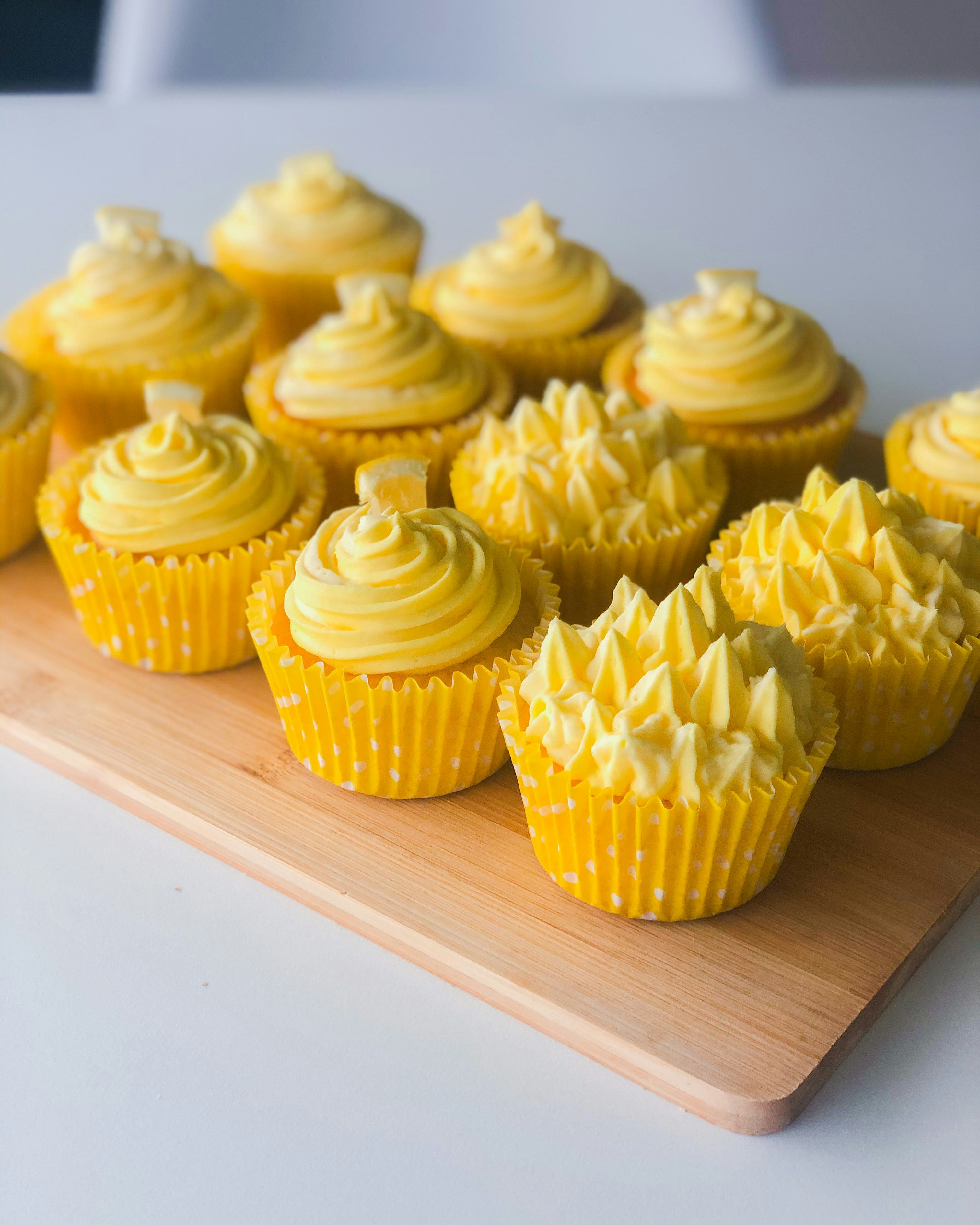 A wooden board topped with yellow cupcakes on top of a table