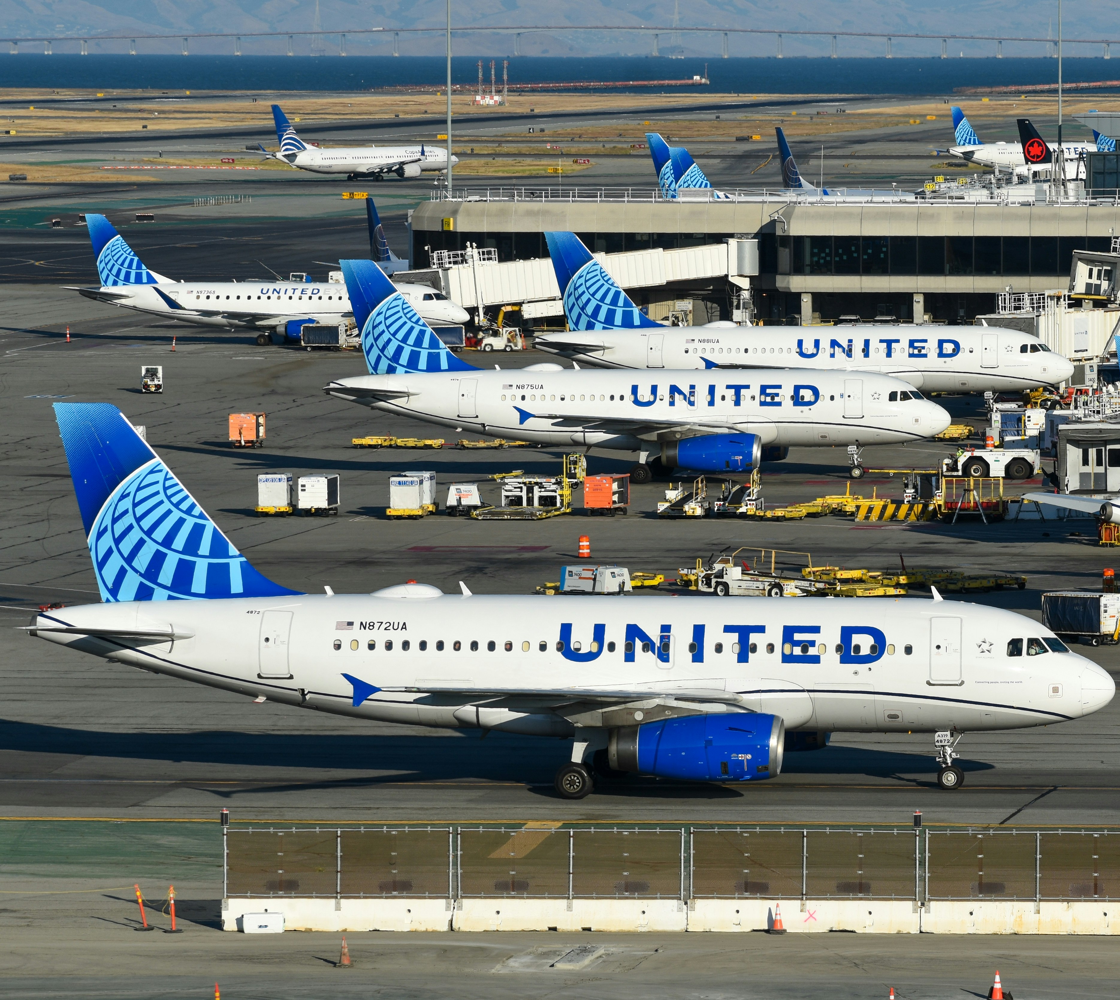 A bunch of airplanes that are on a runway, United Airlines jets at San Francisco
