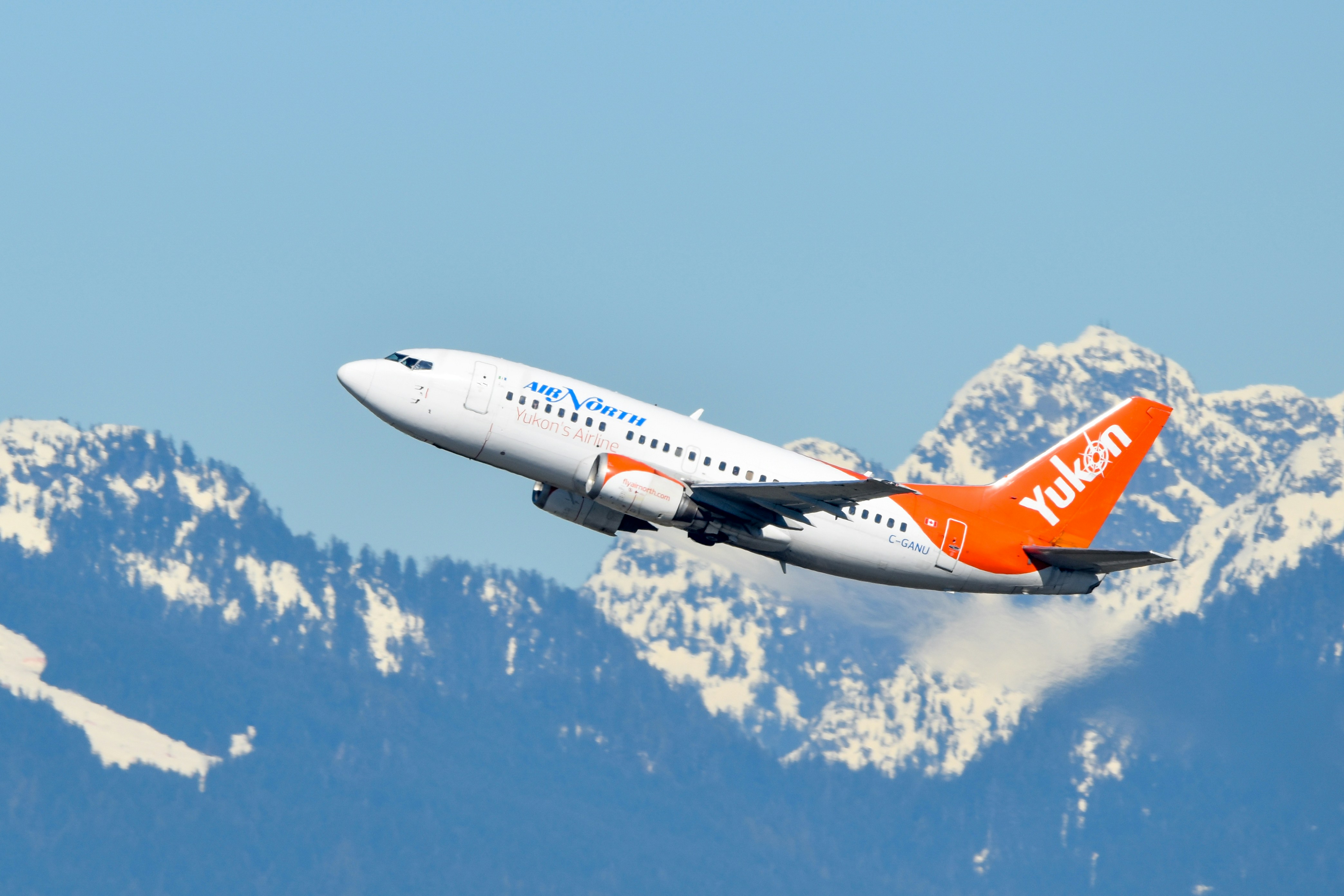An orange and white airplane flying over a mountain range