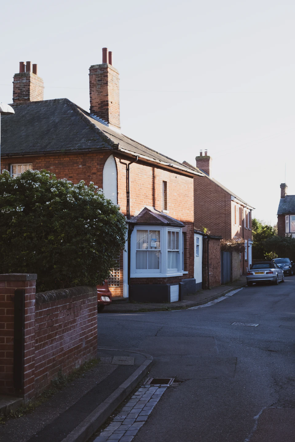 Two brick houses stand side by side with gardens in front of each one