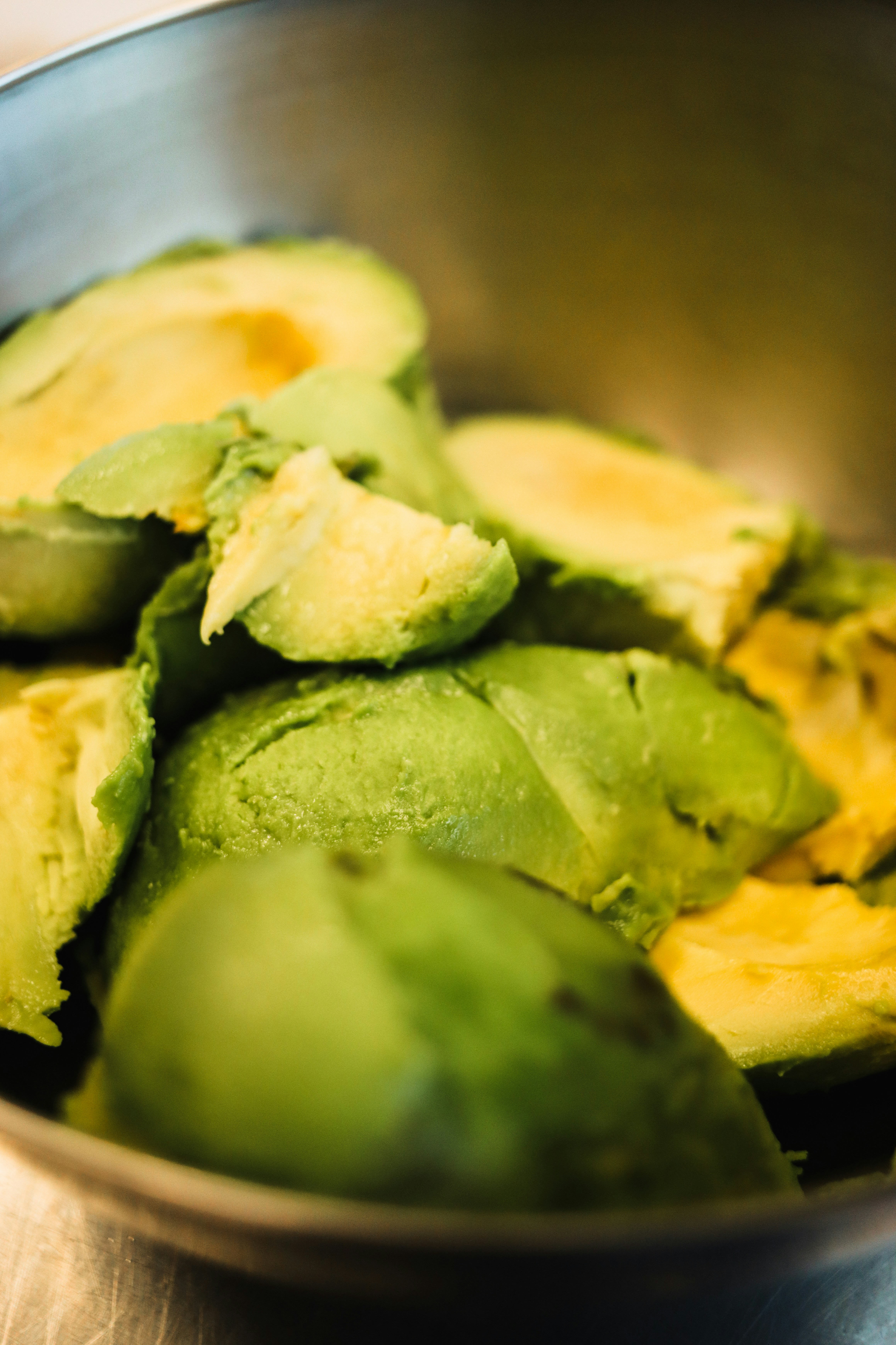 A metal bowl filled with sliced up avocados