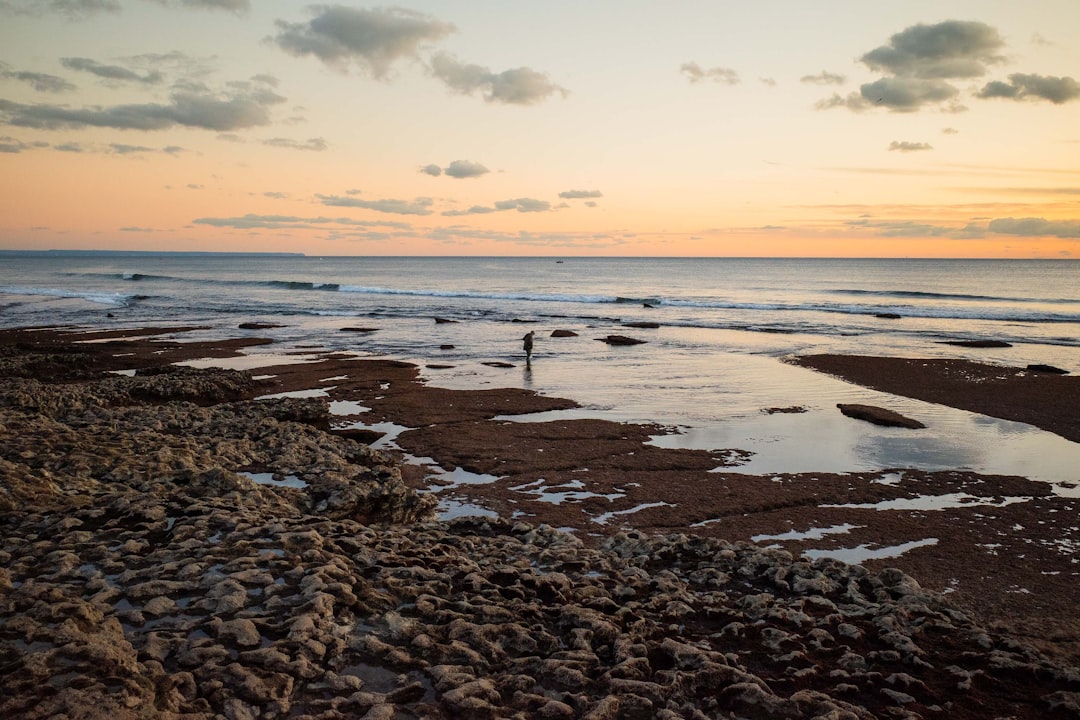 A person standing on a beach at sunset, Lone fisherman on the rocks of Oeiras beach in Portugal.