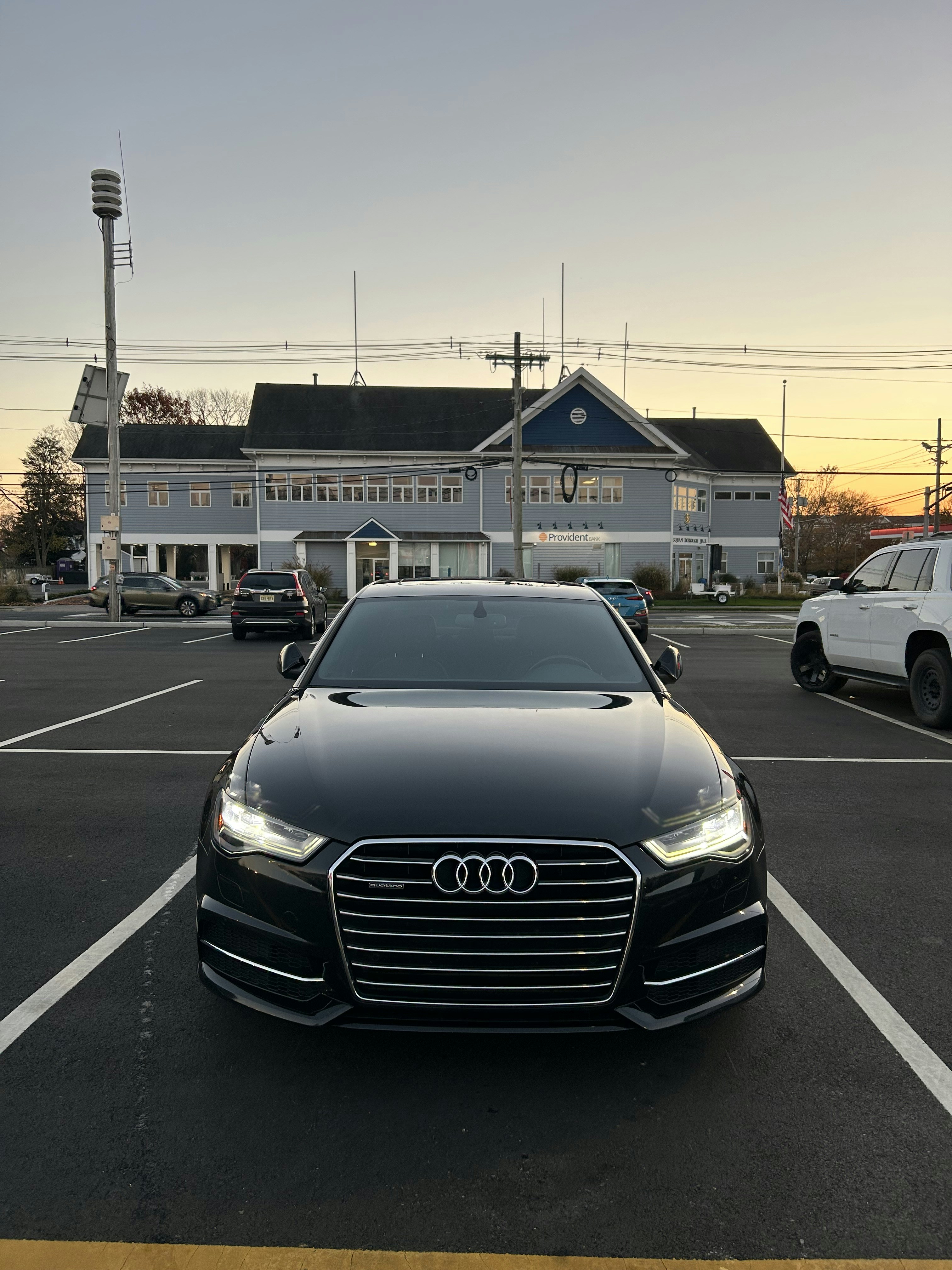 Audi A6 executive sedan in black, parked on city street at dusk, ambient street lighting
