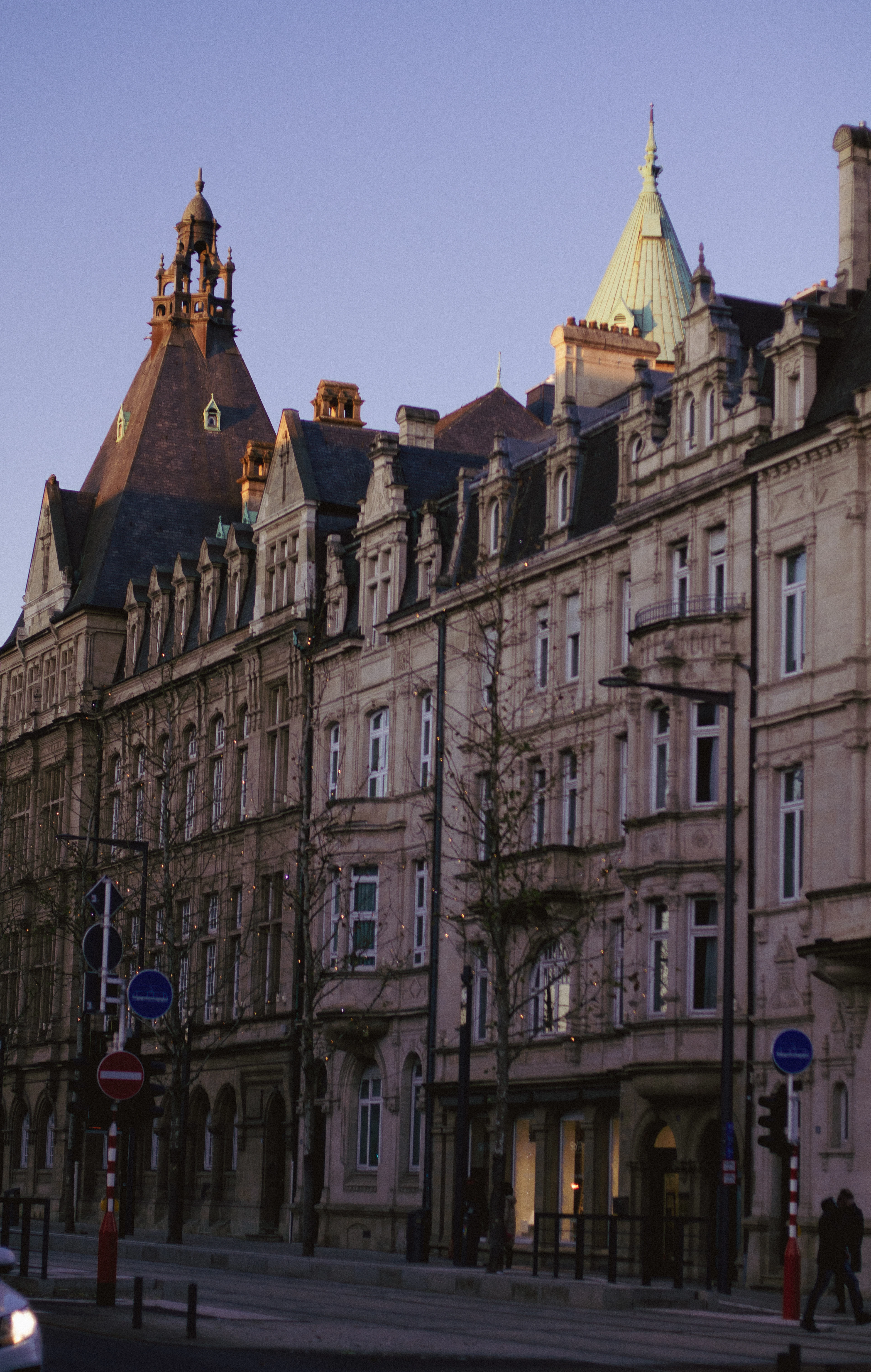 A row of ornate Belle Époque townhouses with turrets lines an empty street at dusk.