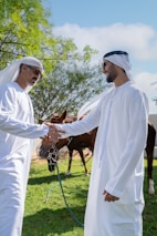Two men shaking hands in front of a horse
