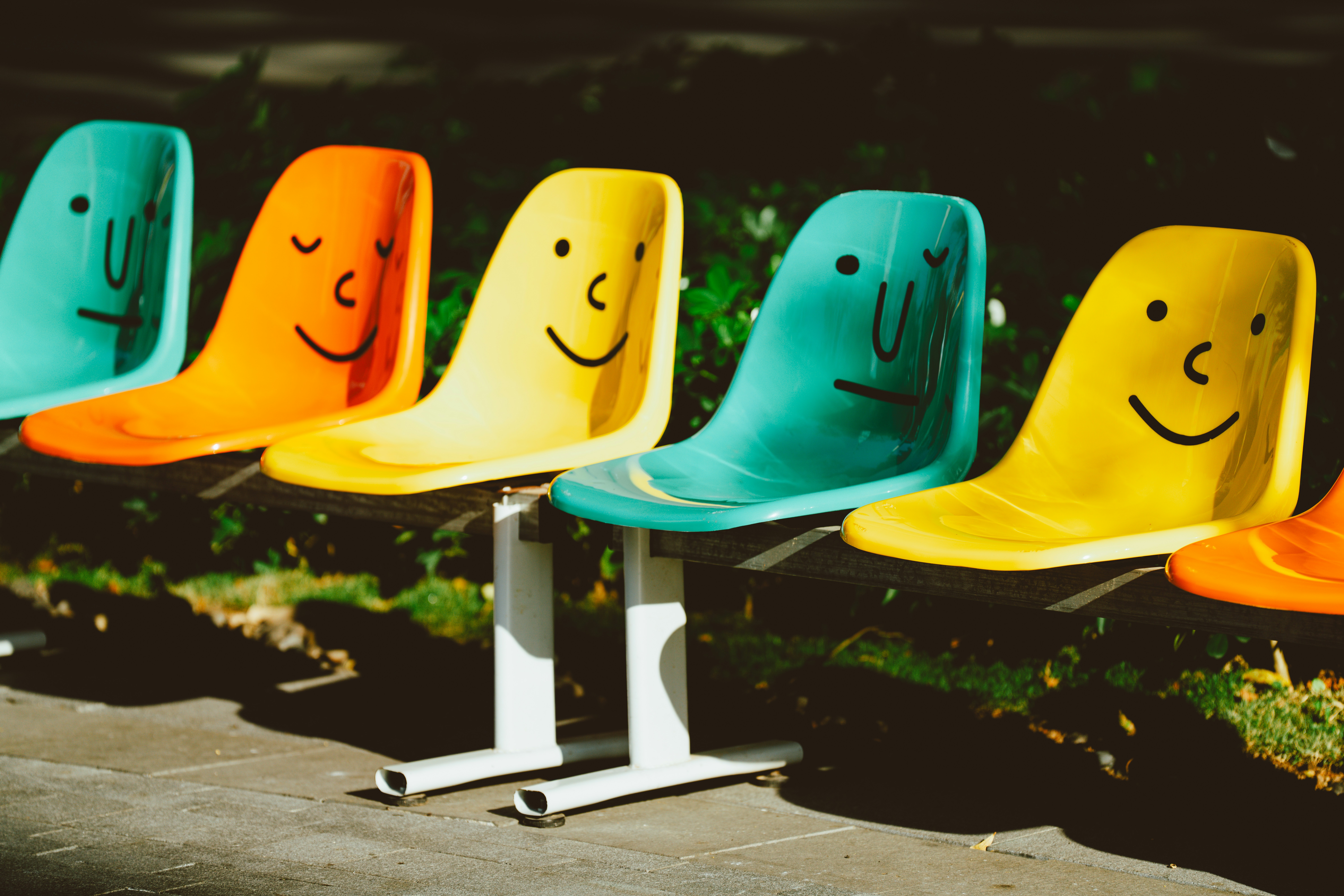 A row of colorful chairs with faces painted on them