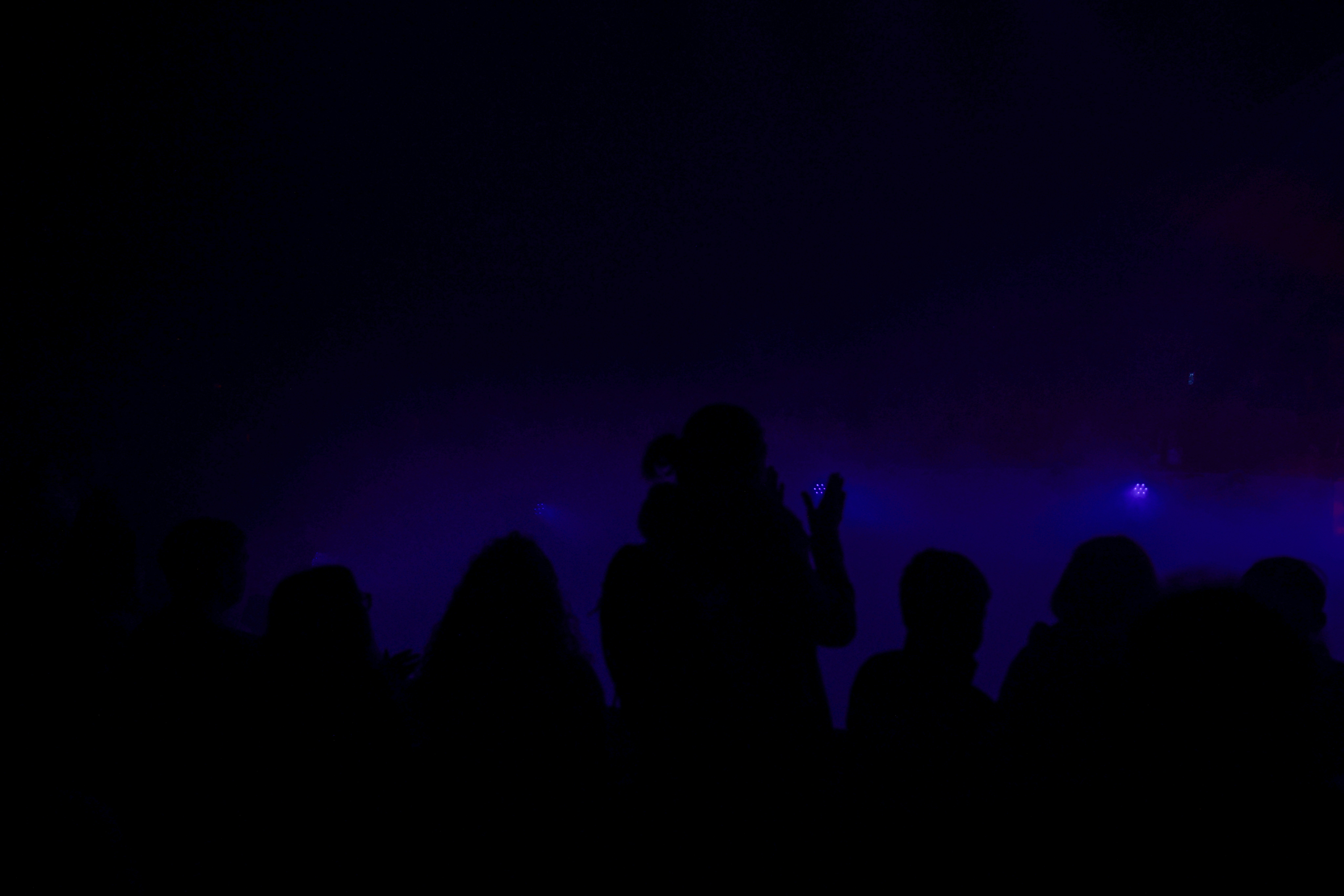 Concert stage with dramatic dark lighting, silhouettes against deep blue haze and dim atmospheric glow