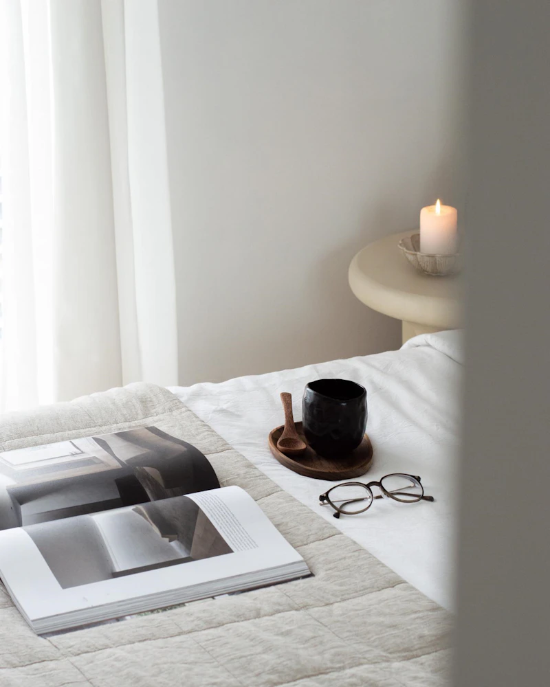 An open magazine, coffee and glasses on a bed