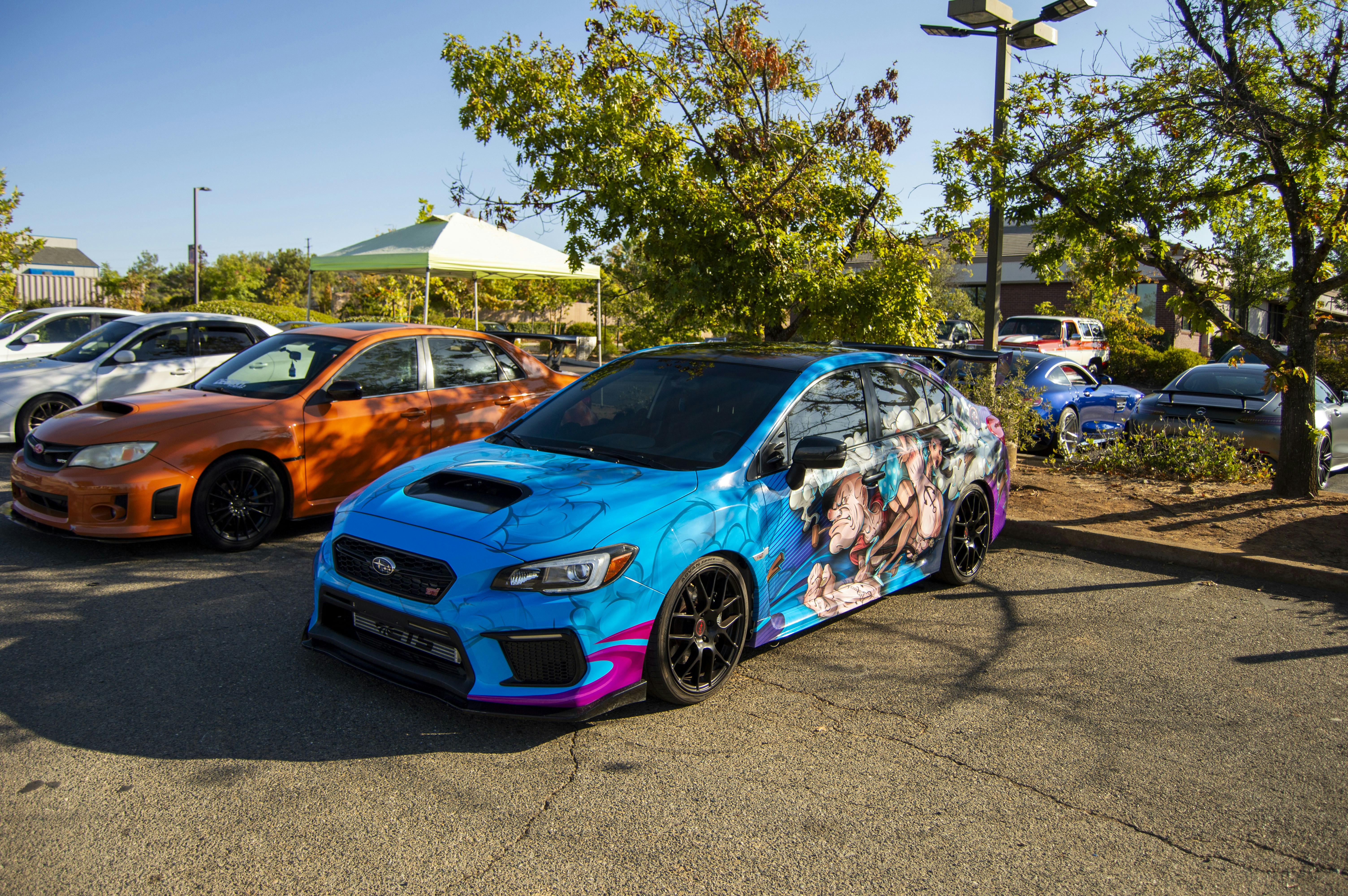 Blue sedan with multicolored character graphics parked outdoors beside other vehicles.
