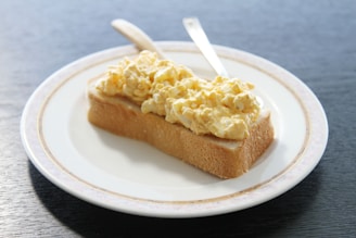 A piece of bread topped with scrambled eggs on a white plate