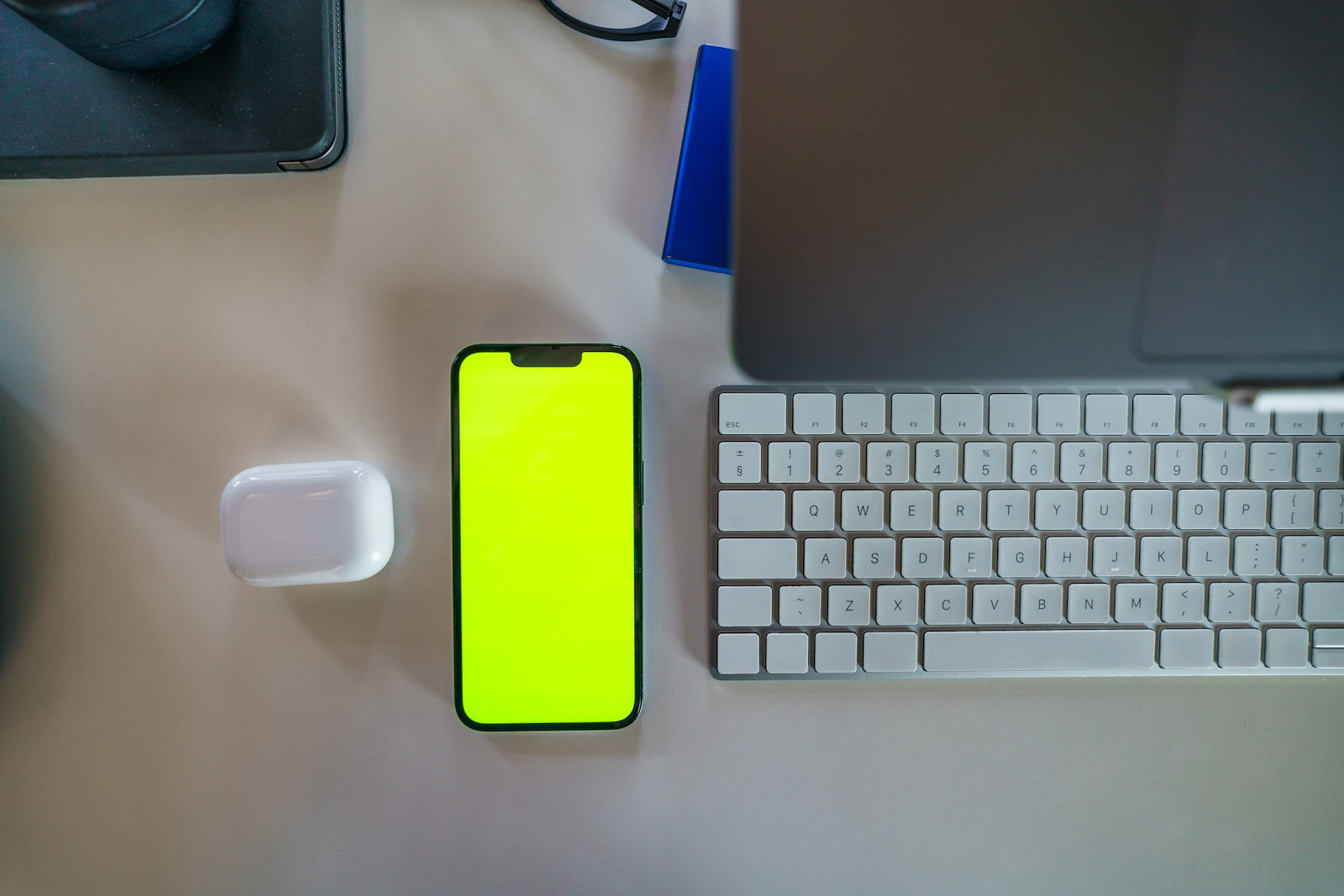 A smartphone with a bright green screen lying on a desk next to a keyboard and earbuds case