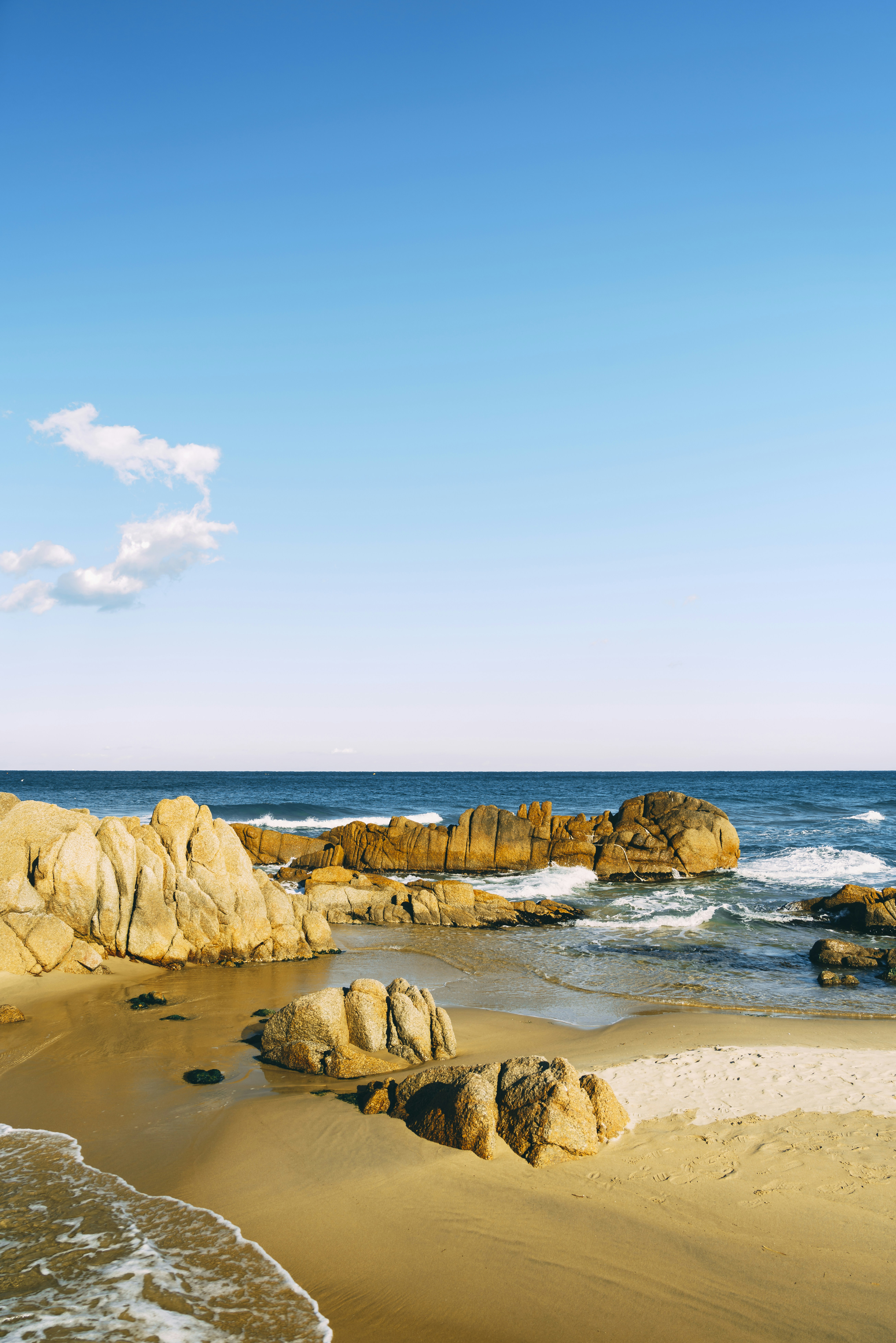 A sandy beach with rocks and water on a sunny day