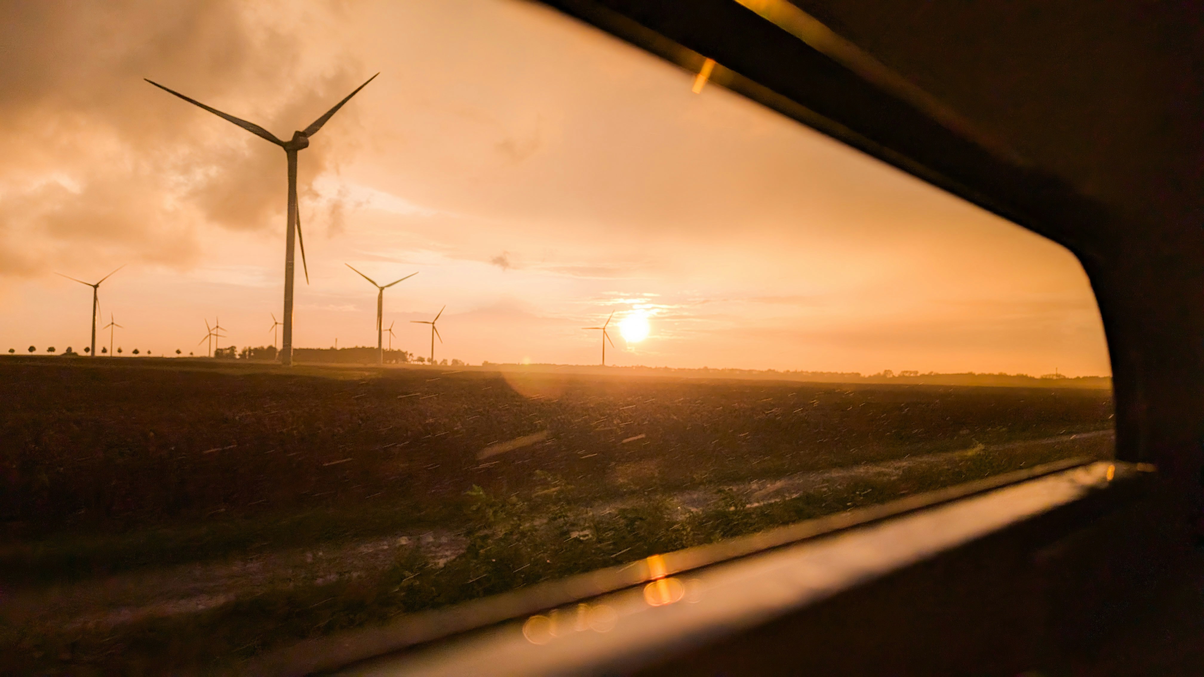 Wind turbines in green field at sunset, warm orange sky, renewable energy landscape