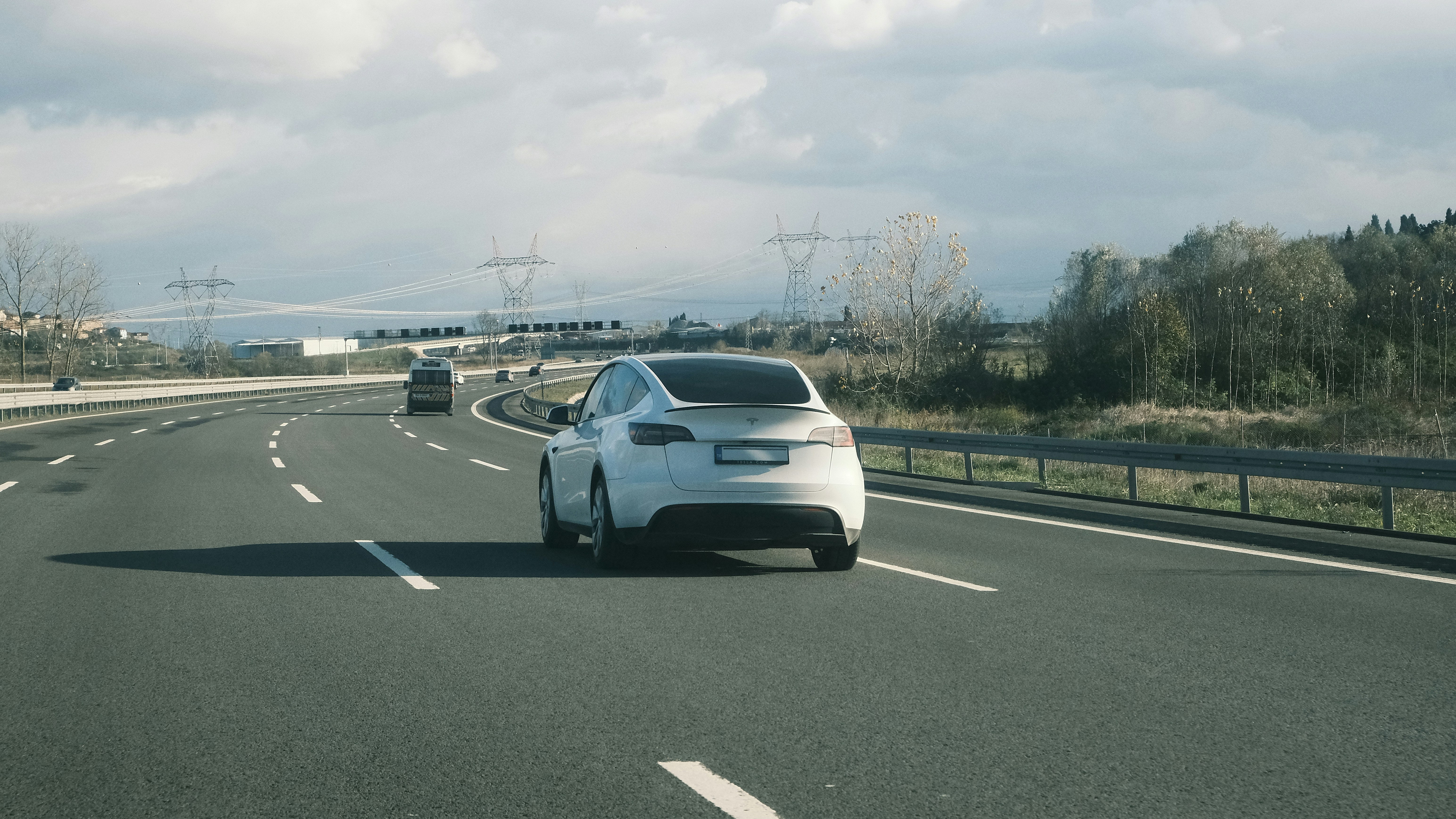 A white car driving down a highway under a cloudy sky