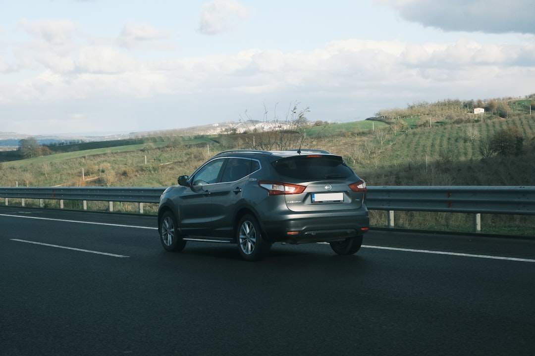 A car driving down a highway next to a lush green hillside,