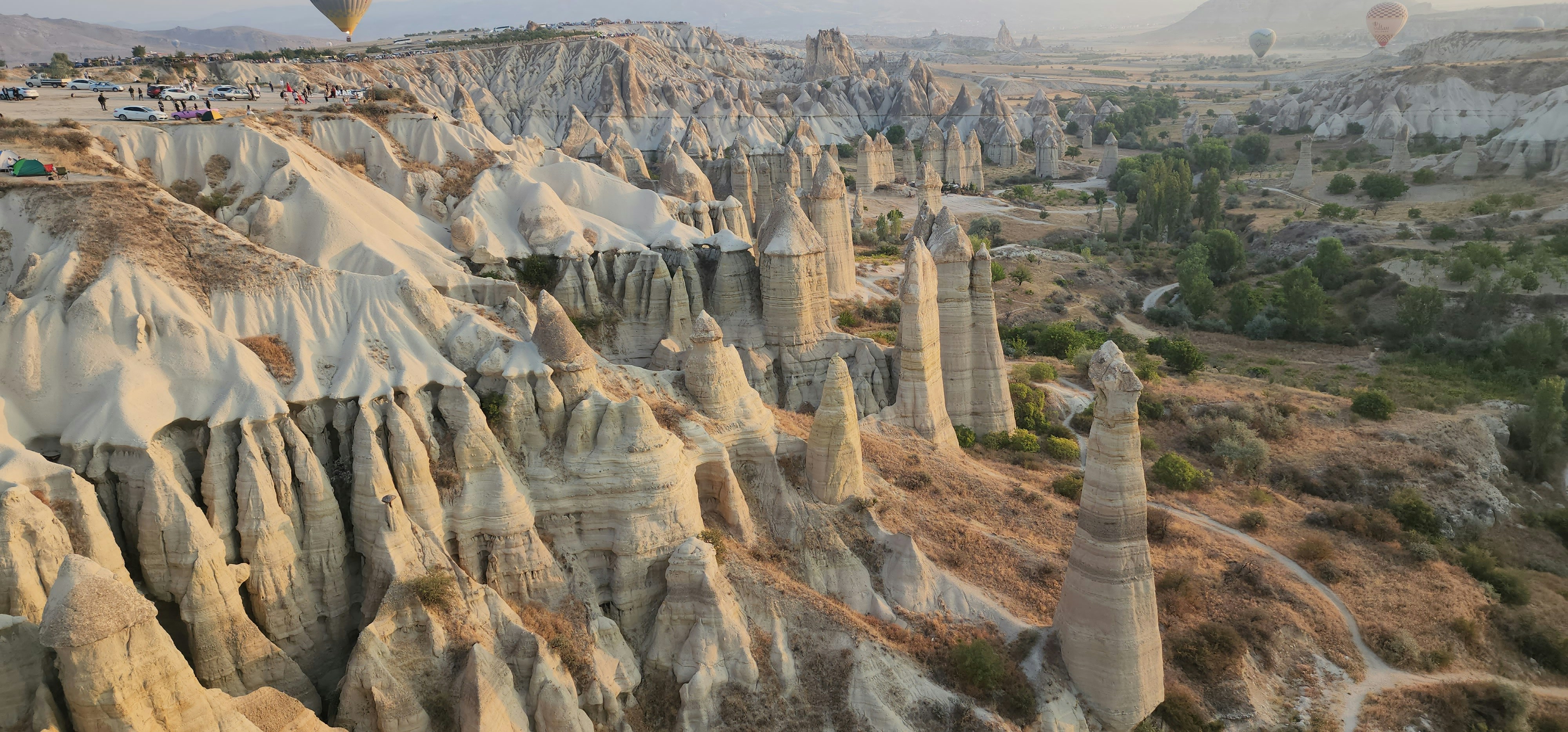 Hot air balloons floating over the fairy chimney rock formations of Cappadocia at sunrise, golden light casting long shadows across the valley