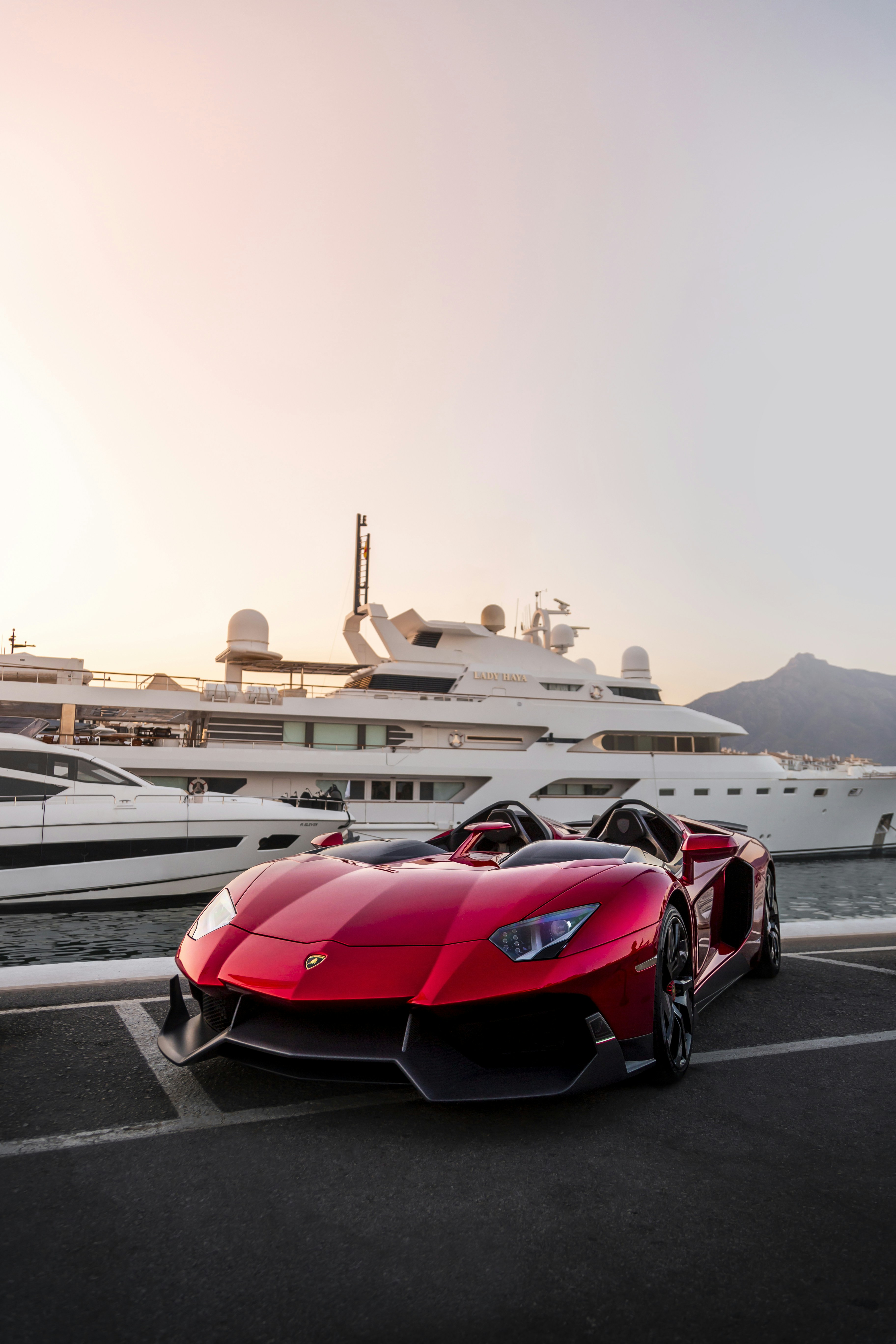 Ein roter Sportwagen, der vor einer Yacht parkt