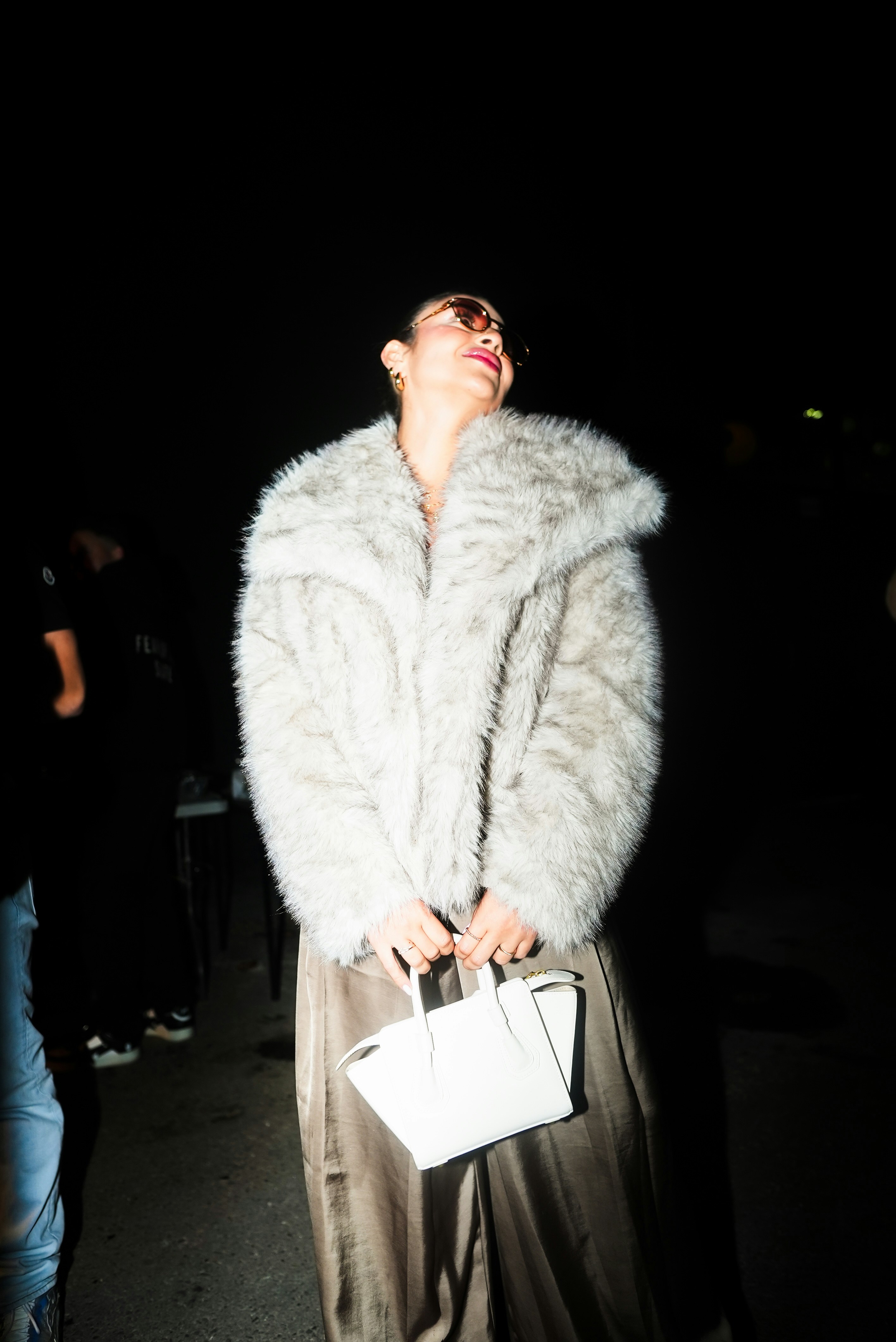 Une femme vêtue d’un manteau de fourrure et tenant un sac à main blanc