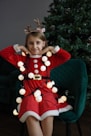 A little girl in a red dress sitting in front of a christmas tree