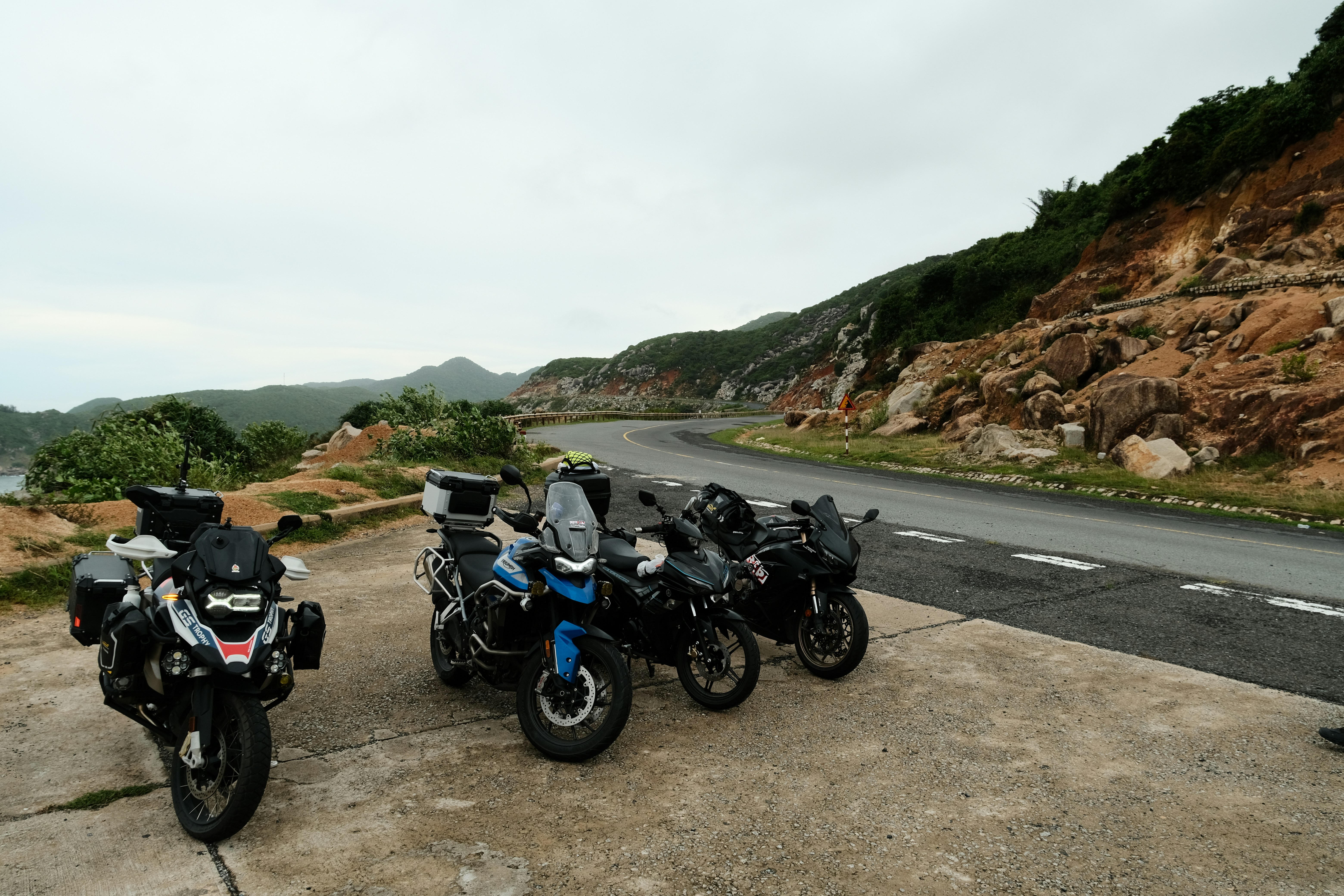 Motorcycle parked on a scenic coastal road in Gokarna, India, with lush green hills in the background