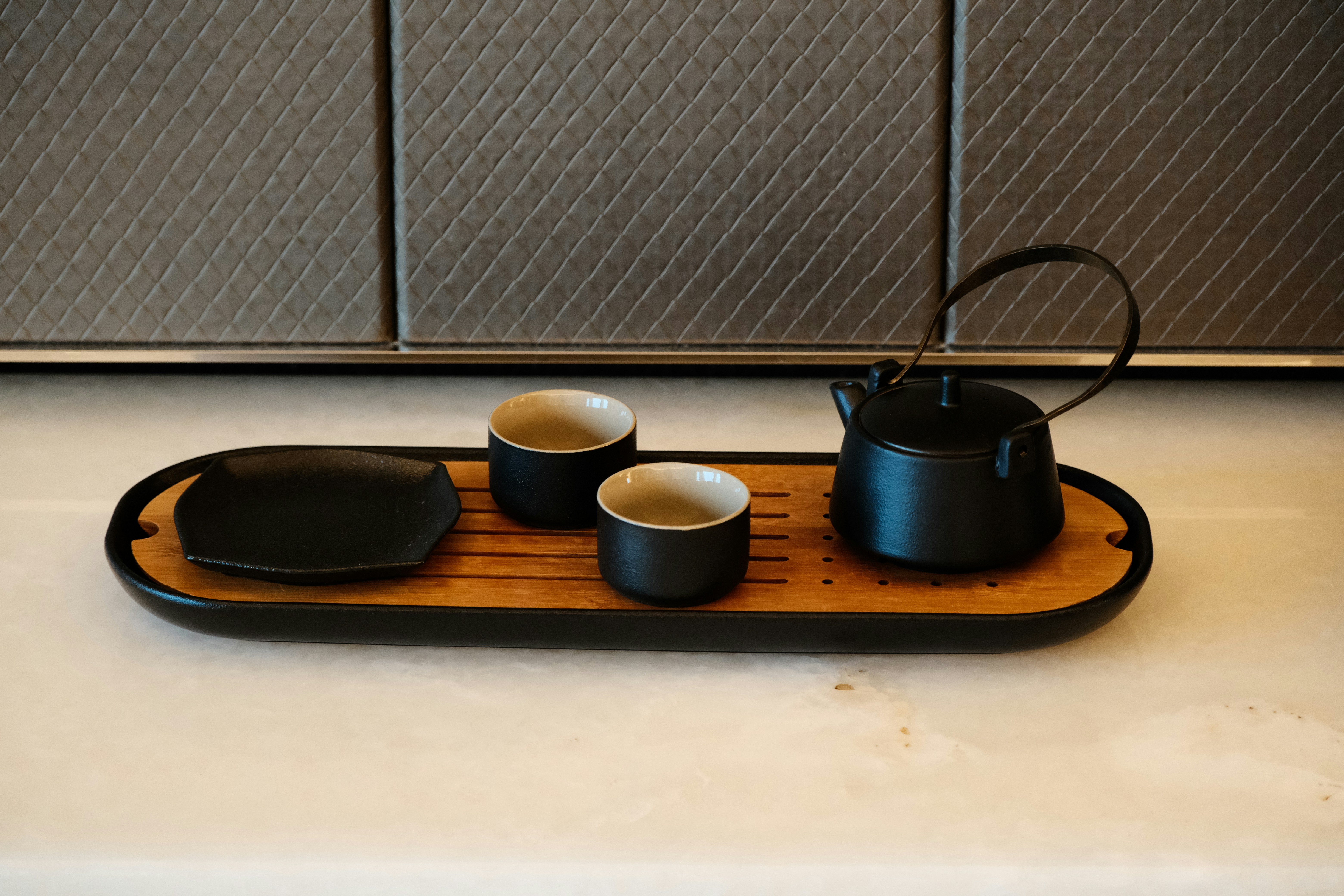 Black cast iron teapot and tea cups on a bamboo tray.
