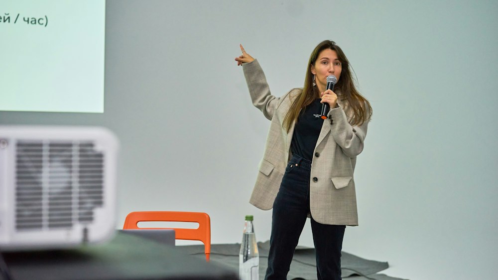 Presenter speaking with a microphone beside a projector