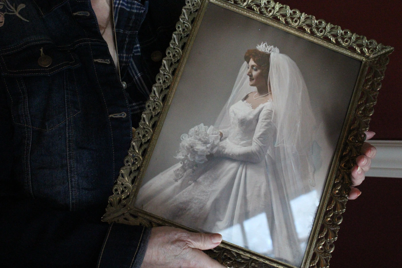 Woman holding a large framed wedding portrait print of a bride in front of a wall