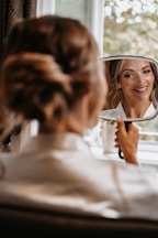A woman in a white shirt is looking at her reflection in a mirror