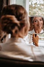 A woman in a white shirt is looking at her reflection in a mirror