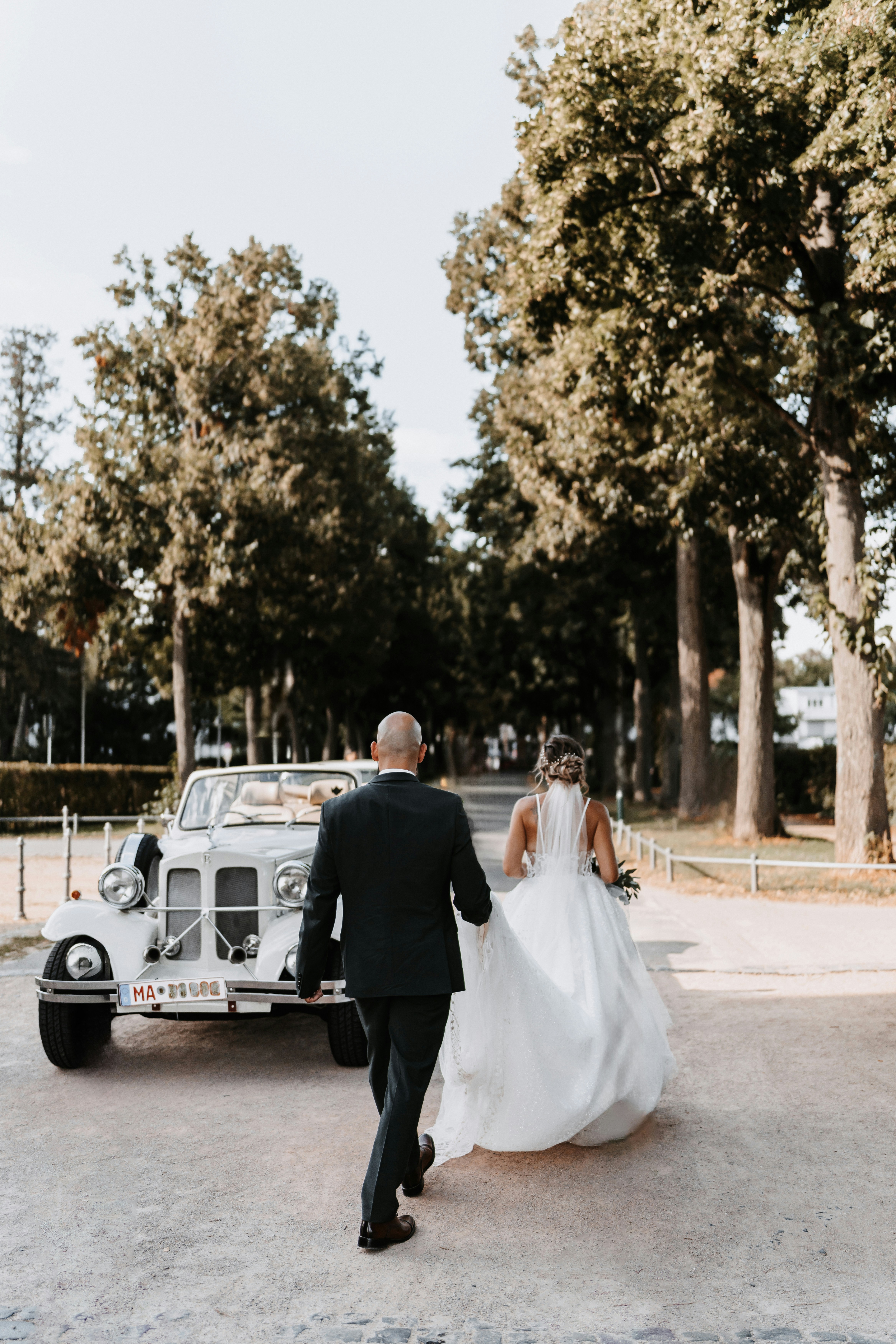 A bride and groom walking towards a vintage car