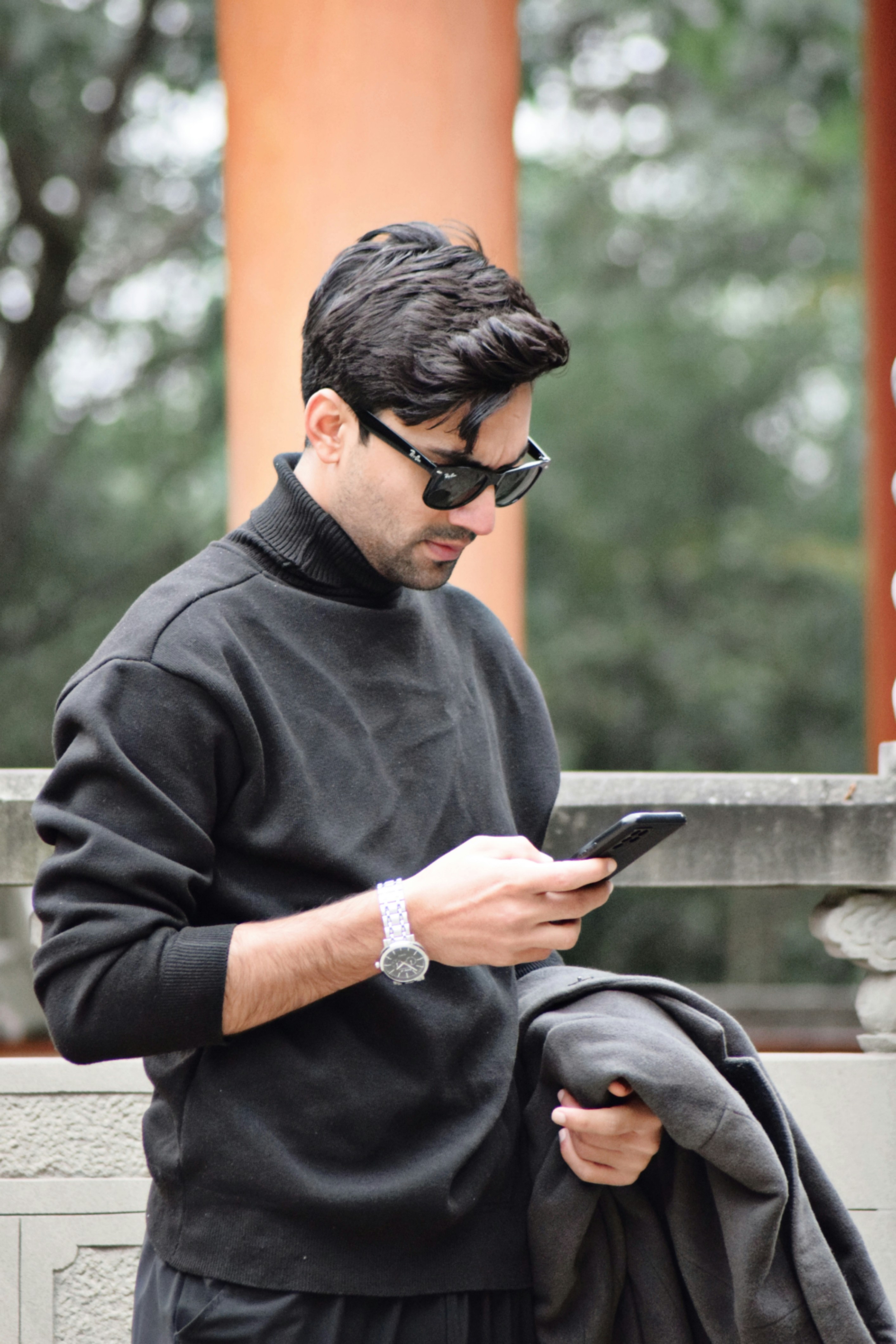 A man in a black outfit looking at his cell phone