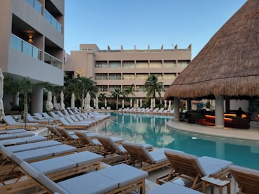 A hotel pool with lounge chairs and a thatched roof