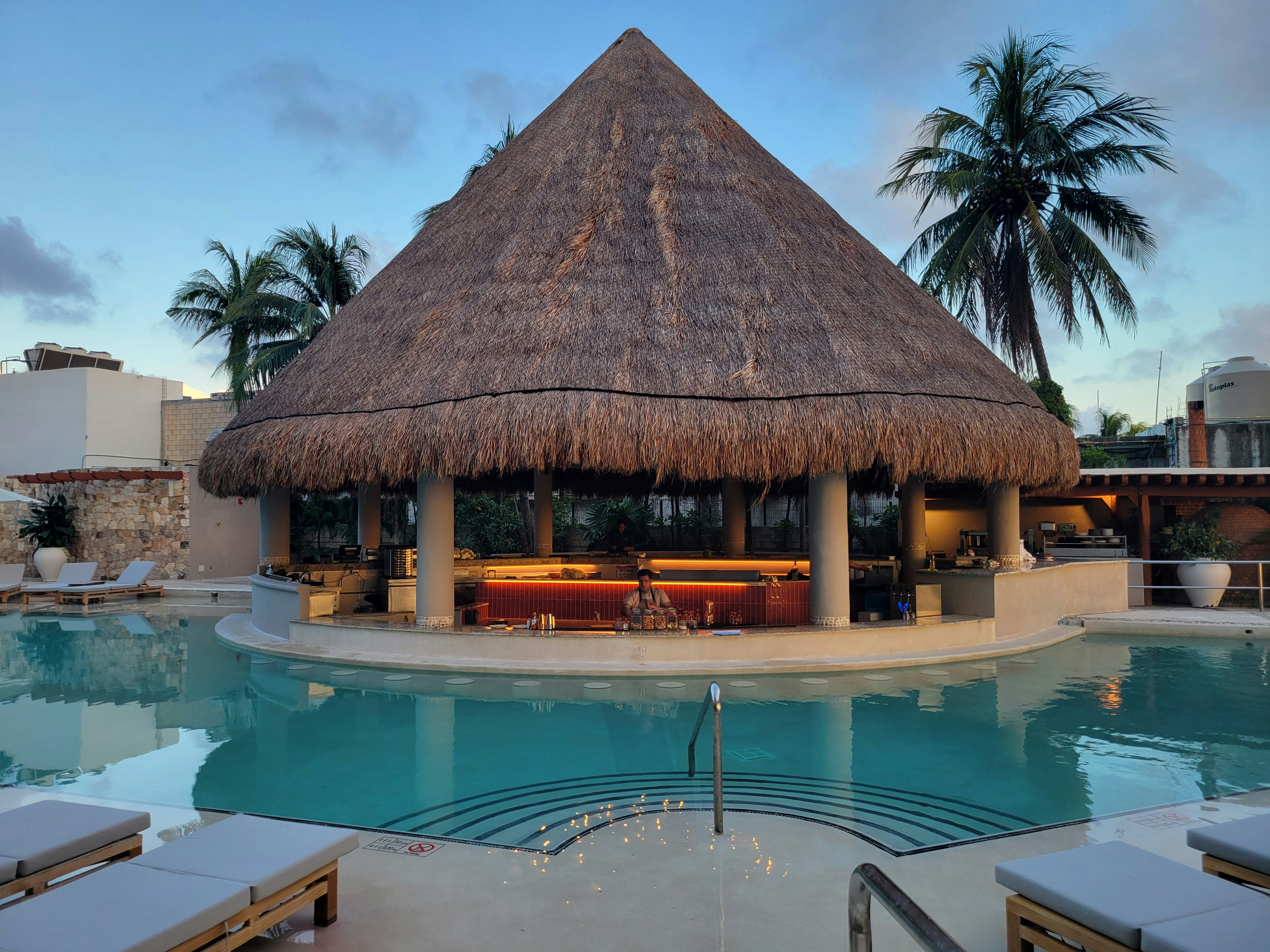 A pool with a thatched roof and lounge chairs, 
