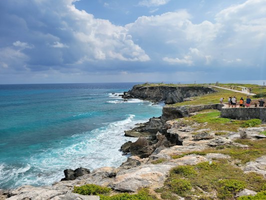 A group of people standing on top of a cliff next to the ocean — Isla Mujeres, Mexico