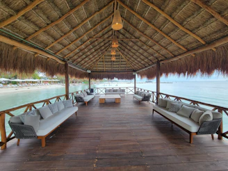 A wooden dock with benches and chairs under a thatched roof