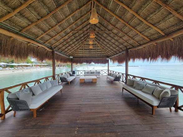 A wooden dock with benches and chairs under a thatched roof