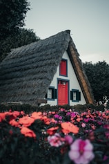 A house with a thatched roof surrounded by flowers