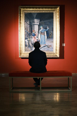 A person sitting on a bench in front of a painting