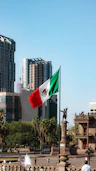 A mexican flag flying in the wind in a city