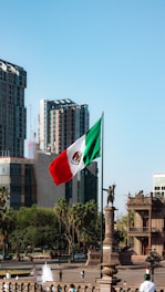 A mexican flag flying in the wind in a city
