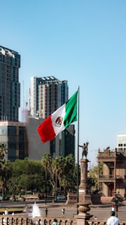 A mexican flag flying in the wind in a city