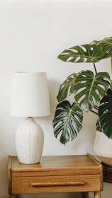 A white vase sitting on top of a wooden table next to a lamp