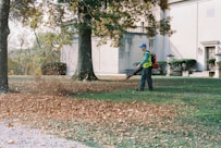 A man with a leaf blower in a yard