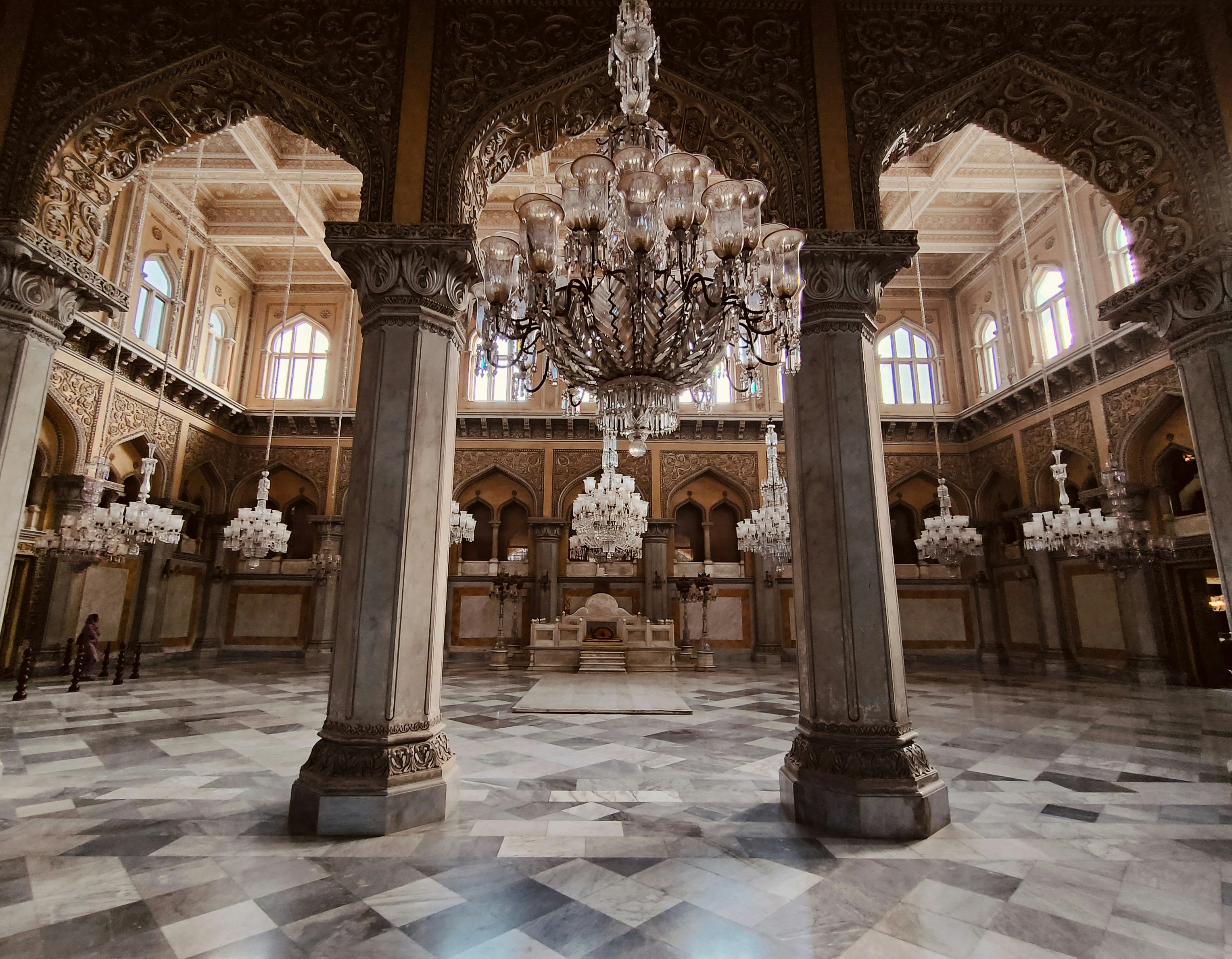 Elegant casino hall with high ornate ceilings, crystal chandeliers casting warm light, polished floors reflecting the glow of gaming machines in a grand architectural space