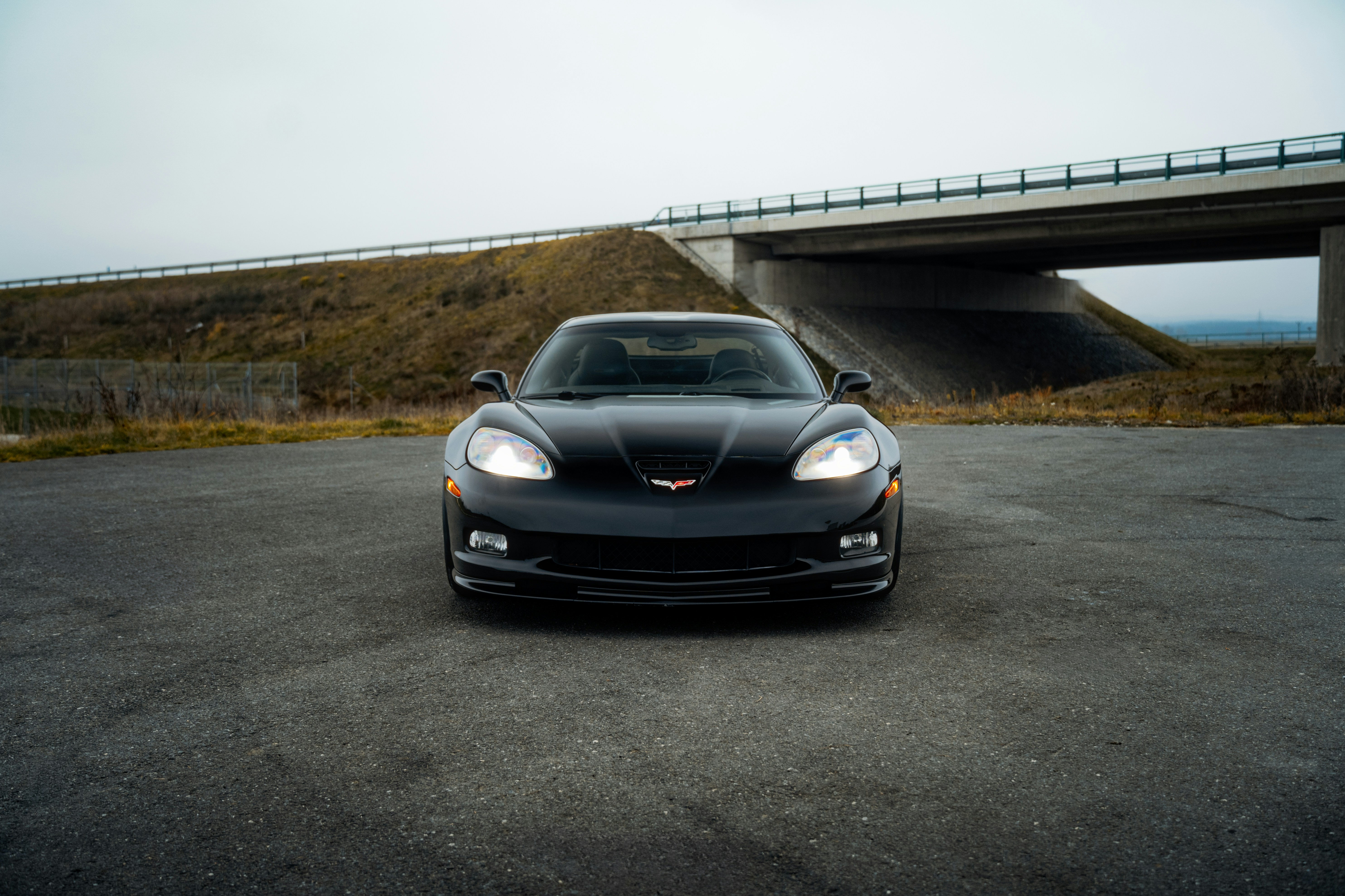A black car parked in a parking lot next to a bridge